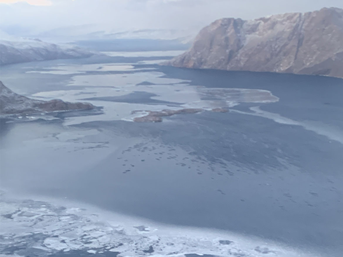 Vue aérienne des eaux glacées de l’océan Arctique et des montagnes au loin.