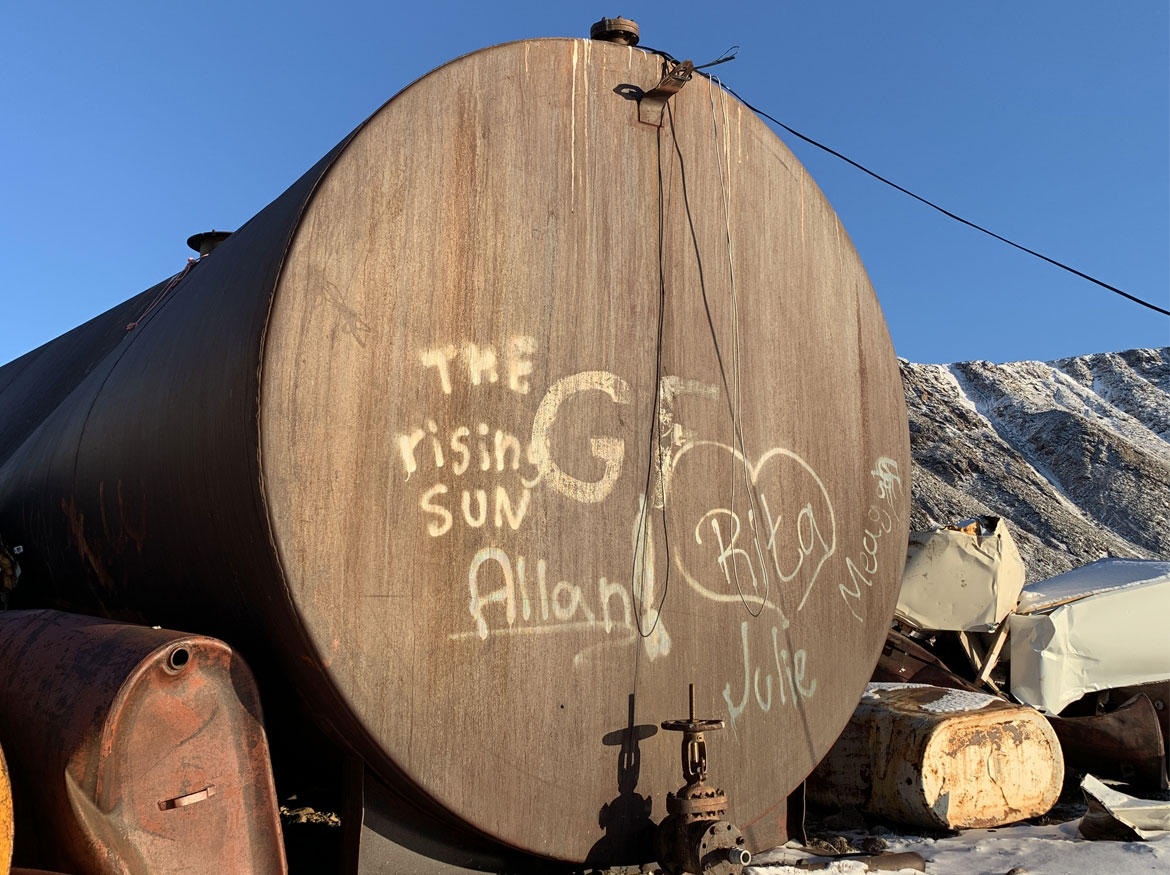 Grand réservoir de diesel et deux plus petits réservoirs d’huile sur un sol enneigé, avec un ciel bleu clair comme toile de fond.