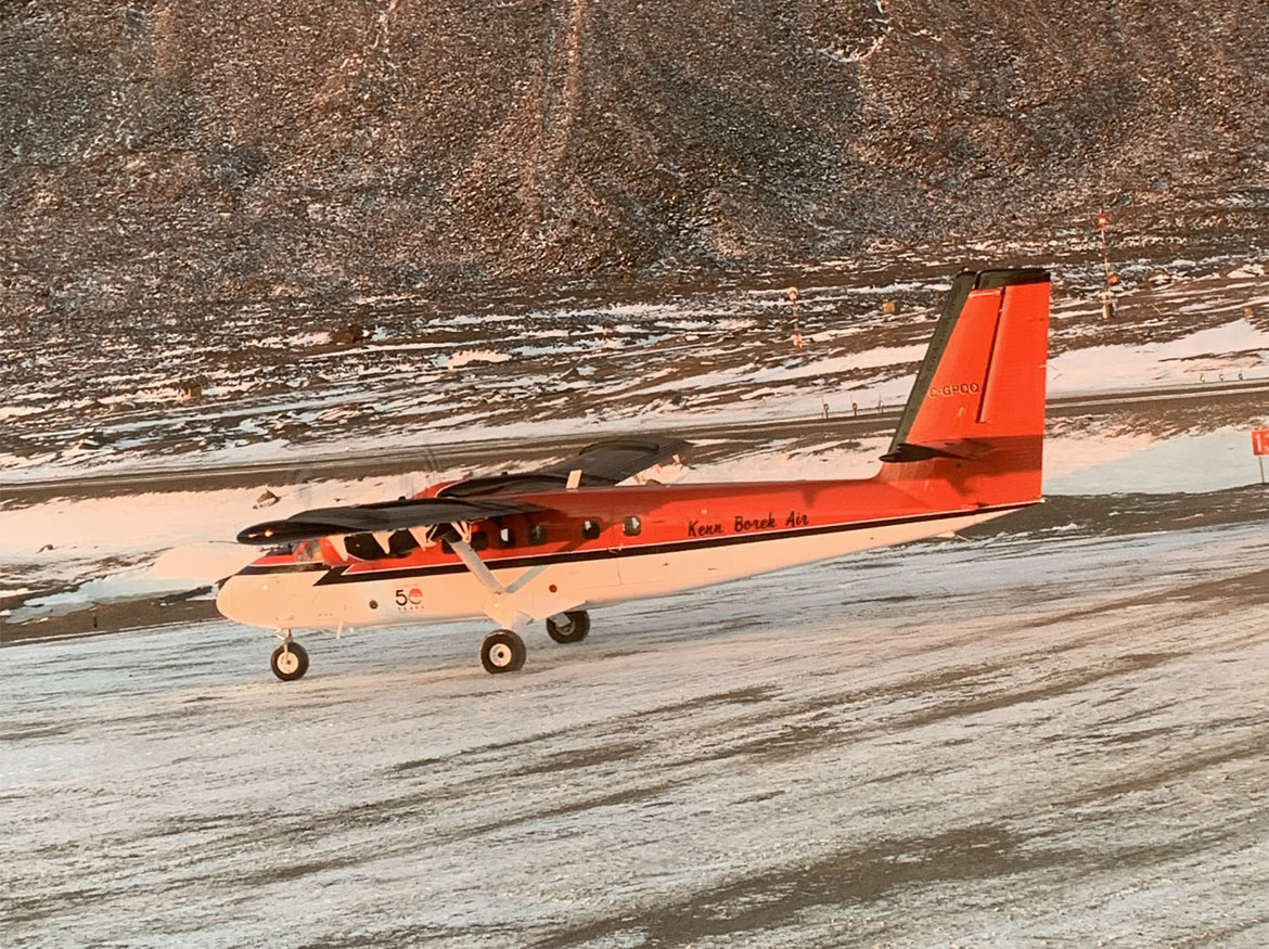 Petit avion de marchandises rouge et blanc sur la glace avec une montagne en arrière-plan.
