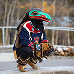 Dancer wearing traditional clothing and a raven mask.