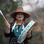 Marilyn dressed in traditional ceremonial clothing playing the drum and singing.