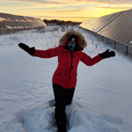 Une participante se tient debout dans la neige, les bras écartés, montrant de longues séries de panneaux solaires de chaque côté d'elle.