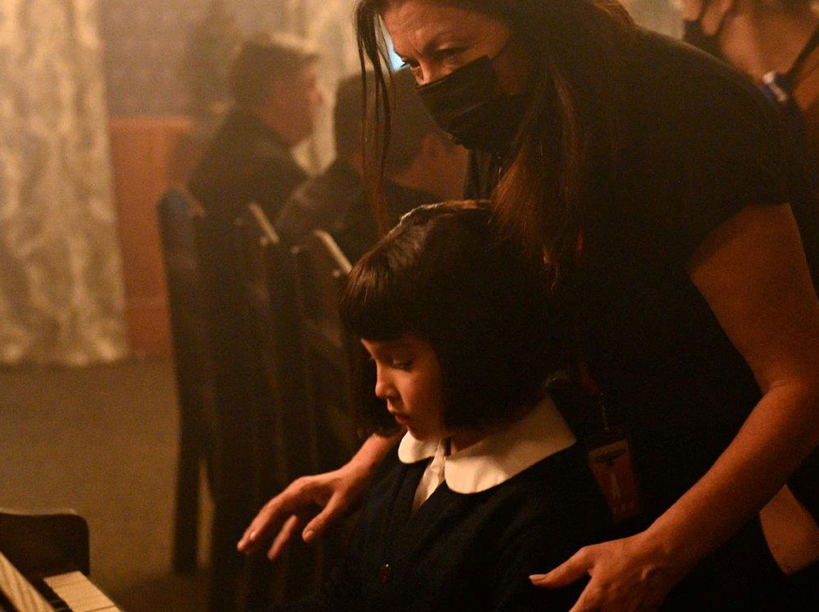 La directrice Marie Clements se tient derrière l'enfant qui joue du piano.