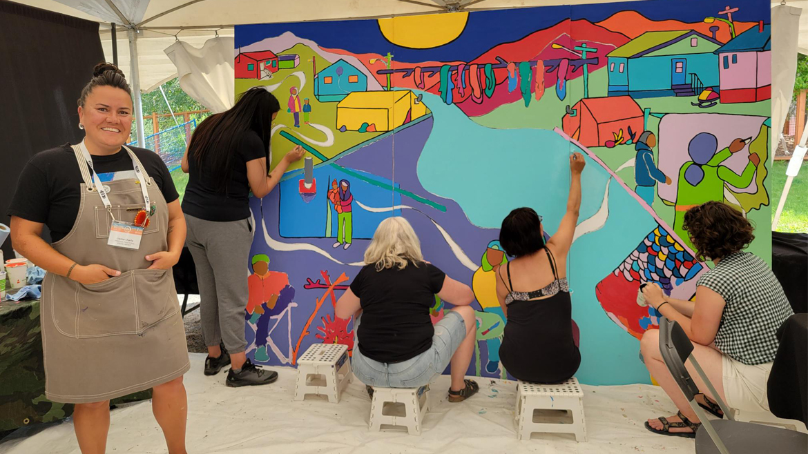 Quatre femmes peignent la murale tandis que l'artiste se tient au premier plan.