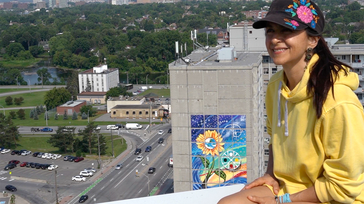 Claudia Salguero, artiste muraliste et pluridisciplinaire, sur un toit surplombant le bâtiment sur lequel est peinte sa fresque.