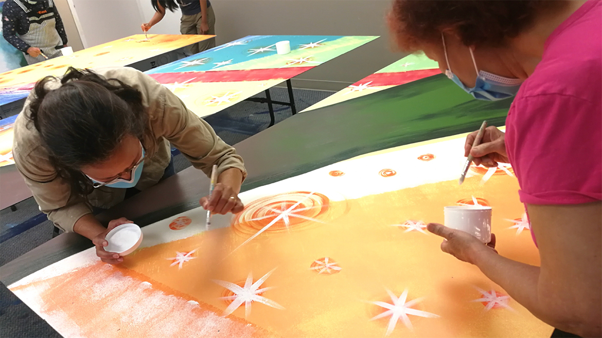 Volunteers wearing surgical face masks painting a mural panel