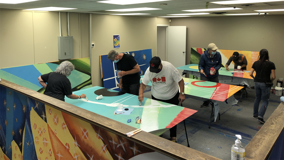 Several small groups of volunteers working on mural panels in a studio