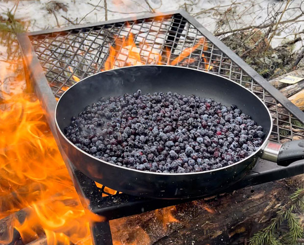 Local blueberries cooking in a frying pan over an outdoor fire.