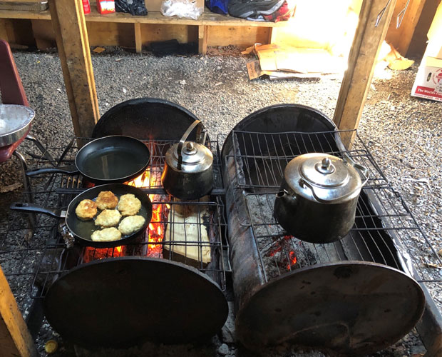Teapots and frying pans containing bannock being heated on wood-fuelled smokers.
