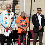 People standing on a stage at Parliament Hill during the 2025 re-raising of the Survivors' Flag ceremony.