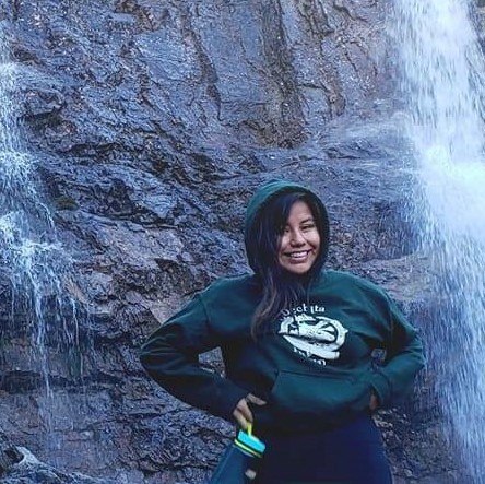 Photography of Sky Lennie standing in front of a rock face with a waterfall flowing down either side of her.