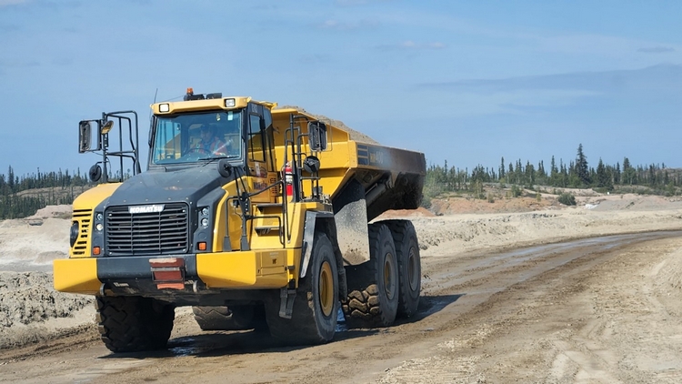 Un camion à pierre articulé roule sur un chemin de terre à travers un chantier.
