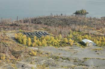 An aerial shot shows several rows of core samples and a low building, separated by trees. Forest burnt by the 2014 forest fires is visible behind the structures.