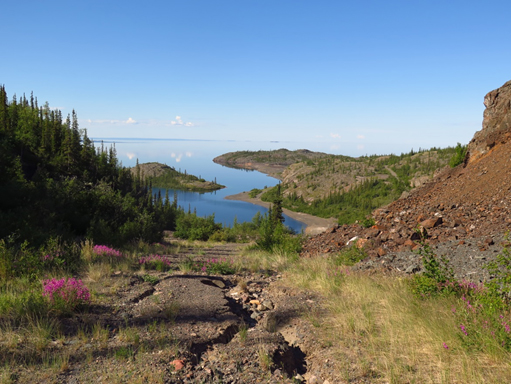 A deteriorating dirt road leads down to the main Port Radium site with Great Bear Lake in the background.