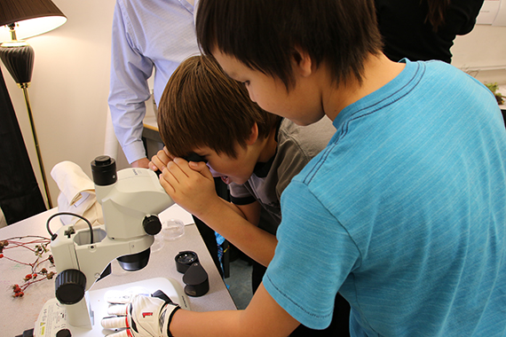 Un étudiant examine au microscope un échantillon tenu par son ami.