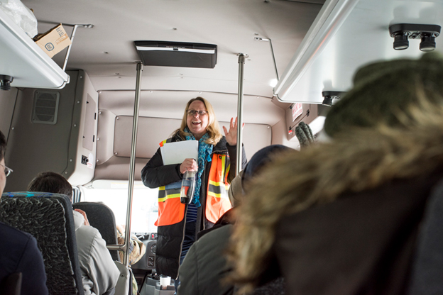 Cette photo montre une femme portant un équipement de protection personnelle au cours d'un voyage en autobus avec d'autres personnes portant un équipement de protection personnelle.