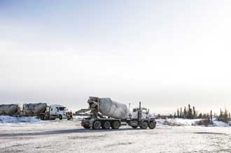 This picture shows a cement mixing truck driving down a snowy road on the former mine site. Workers and other mixing trucks are visible in the background.