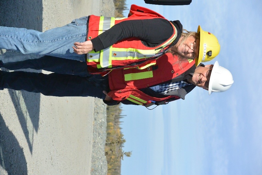 Une femme et un homme, tous deux souriants, portant un équipement de protection individuelle se trouvent sur une surface plane de gravier, sur le site de la mine Giant.